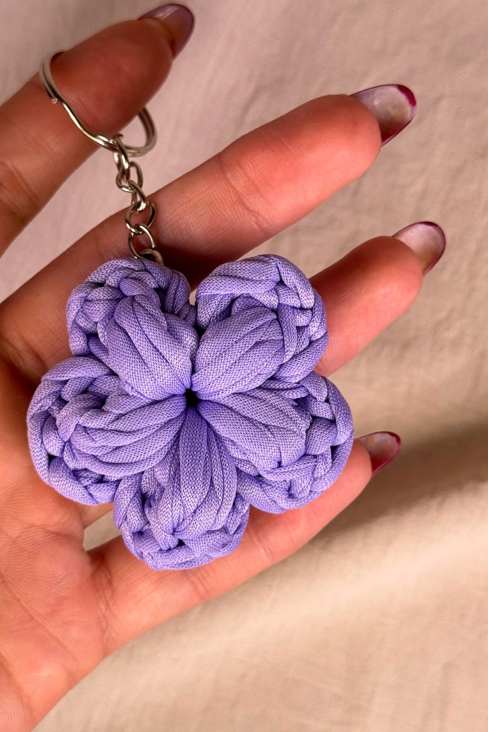Portachiavi a fiore lilla in fettuccia all’uncinetto, fatto a mano in Italia da Made By Hand, mostrato in mano per dare un’idea della grandezza