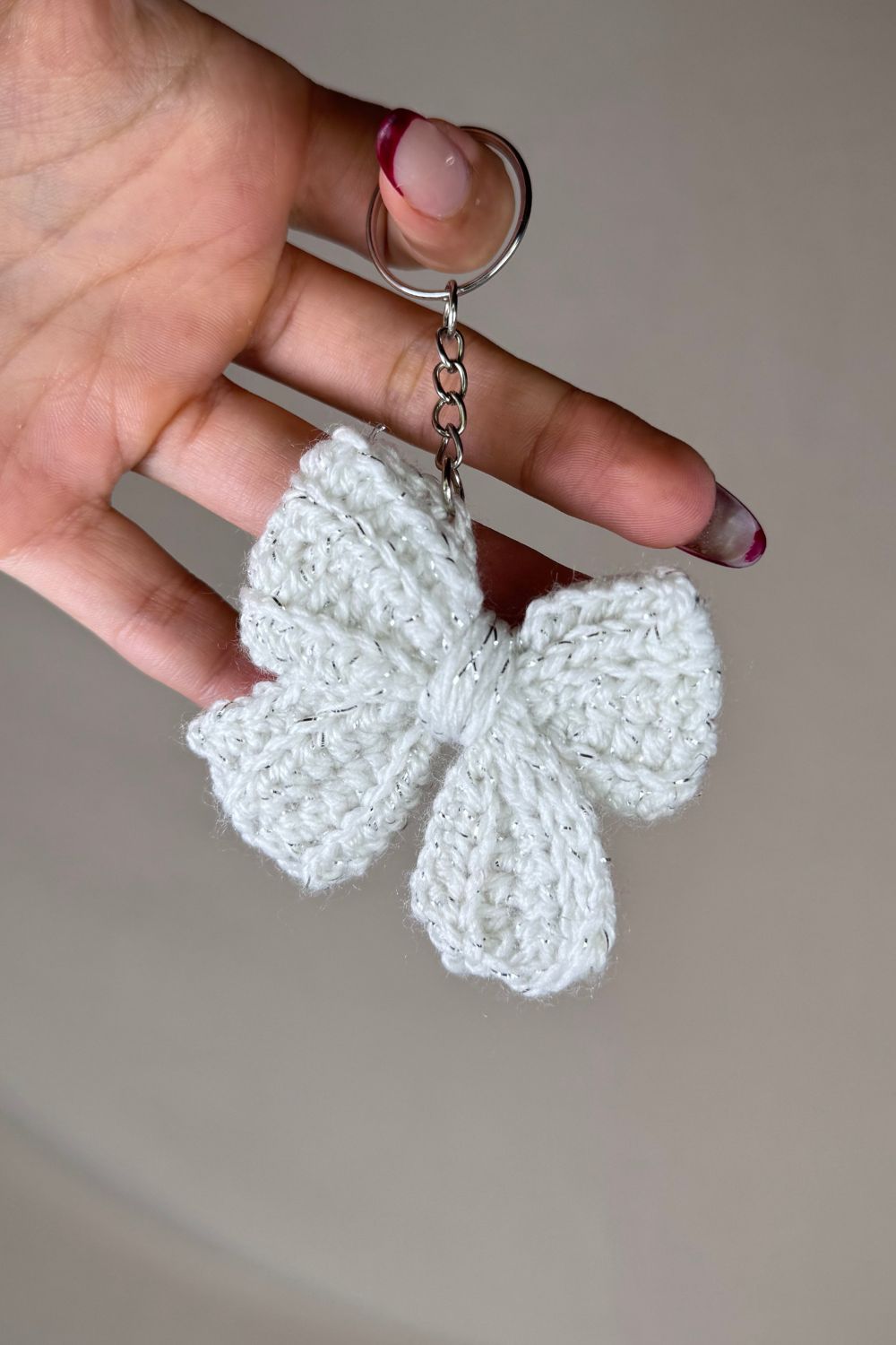 Portachiavi a fiocco bianco realizzato all’uncinetto, fatto a mano in Italia da Made By Hand, mostrato in mano per evidenziare i dettagli artigianali e la dimensione reale