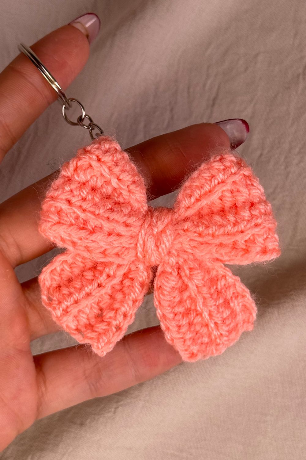Portachiavi a fiocco rosa salmone realizzato all’uncinetto, fatto a mano in Italia da Made By Hand, mostrato in mano per evidenziare i dettagli artigianali e la dimensione reale