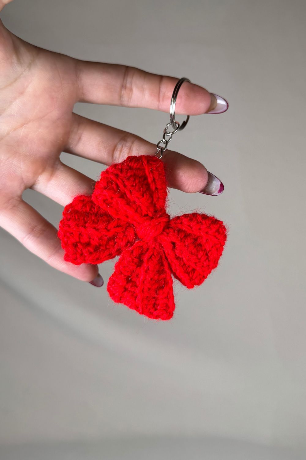 Portachiavi a fiocco rosso realizzato all’uncinetto, fatto a mano in Italia da Made By Hand, mostrato in mano per evidenziare i dettagli artigianali e la dimensione reale