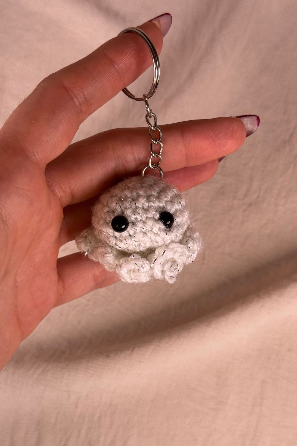 Portachiavi Polpetto bianco all’uncinetto artigianale Made By Hand tenuto in mano per mostrare le dimensioni reali, realizzato a mano con filato di qualità Made in Italy.