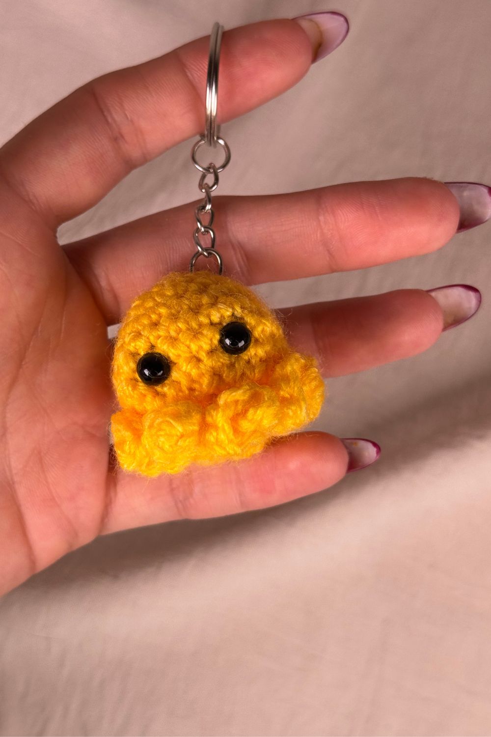 Portachiavi Polpetto giallo all’uncinetto artigianale Made By Hand tenuto in mano per mostrare le dimensioni reali, realizzato a mano con filato di qualità Made in Italy.
