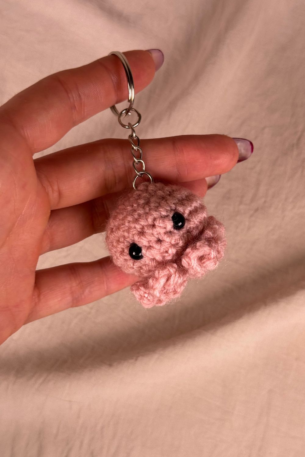 Portachiavi Polpetto rosa all’uncinetto artigianale Made By Hand tenuto in mano per mostrare le dimensioni reali, realizzato a mano con filato di qualità Made in Italy.