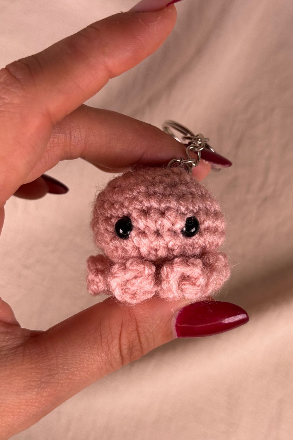 Portachiavi Polpetto rosa all’uncinetto artigianale Made By Hand tenuto in mano per mostrare le dimensioni reali, realizzato a mano con filato di qualità Made in Italy.