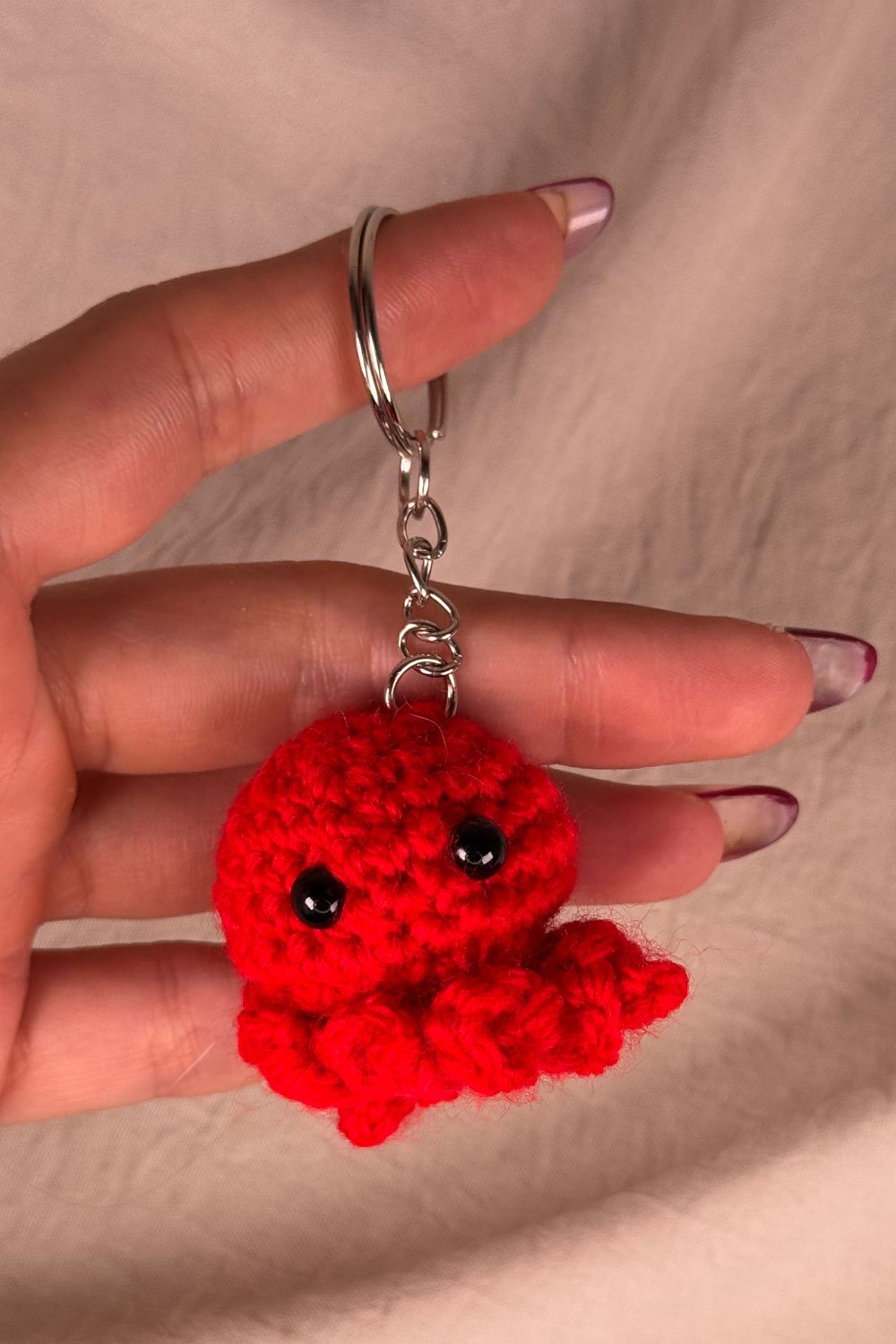 Portachiavi Polpetto rosso all’uncinetto artigianale Made By Hand tenuto in mano per mostrare le dimensioni reali, realizzato a mano con filato di qualità Made in Italy.