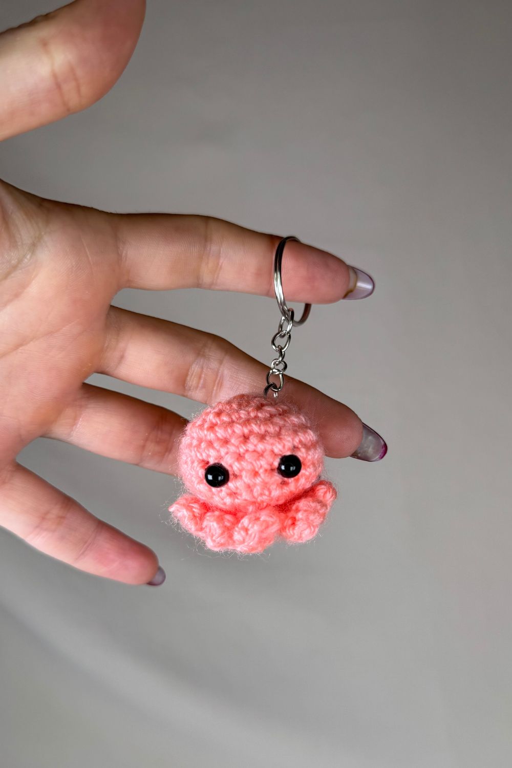 Portachiavi Polpetto salmone all’uncinetto artigianale Made By Hand tenuto in mano per mostrare le dimensioni reali, realizzato a mano con filato di qualità Made in Italy.