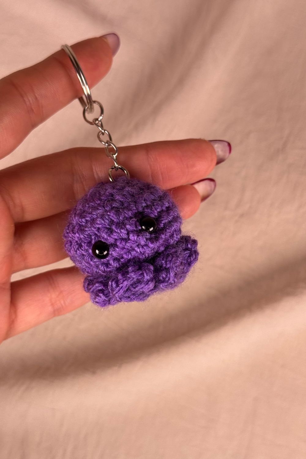 Portachiavi Polpetto viola all’uncinetto artigianale Made By Hand tenuto in mano per mostrare le dimensioni reali, realizzato a mano con filato di qualità Made in Italy.
