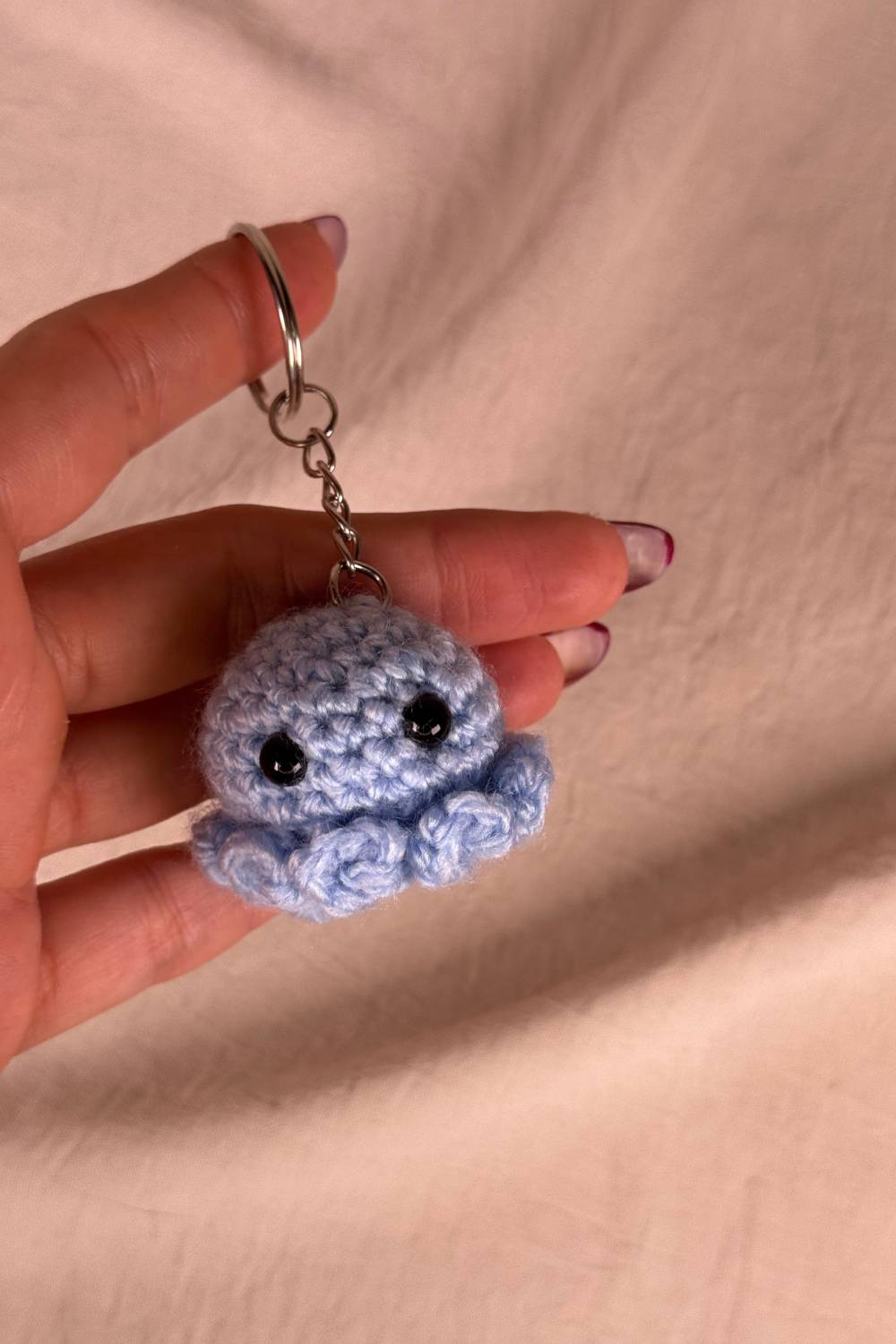 Portachiavi Polpetto azzurro all’uncinetto artigianale Made By Hand tenuto in mano per mostrare le dimensioni reali, realizzato a mano con filato di qualità Made in Italy.