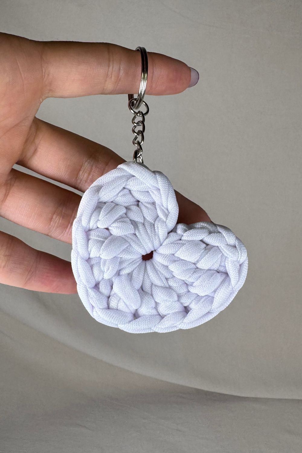 Portachiavi a cuore bianco fatto a mano in Italia da Made By Hand, in fettuccia lavorata all’uncinetto, mostrato in mano per farne vedere la grandezza