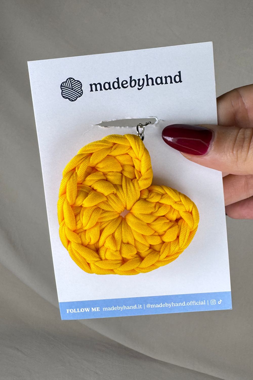 Portachiavi cuore giallo Made By Hand, in fettuccia all’uncinetto, confezionato su cartoncino bianco con logo, perfetto come bomboniera solare e artigianale
