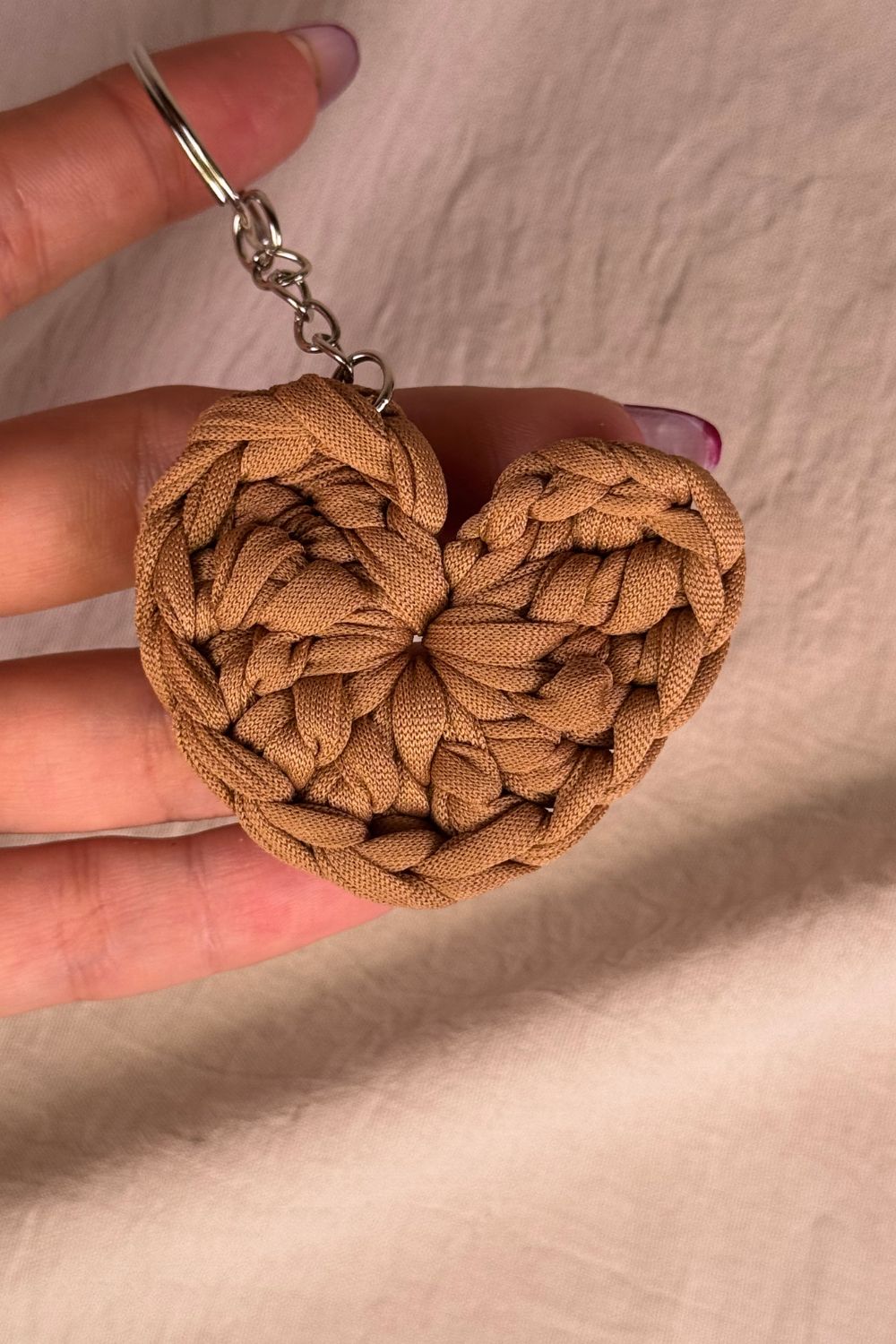 Portachiavi cuore color nocciola in fettuccia all’uncinetto, realizzato a mano in Italia da Made By Hand, mostrato in mano per evidenziare la misura