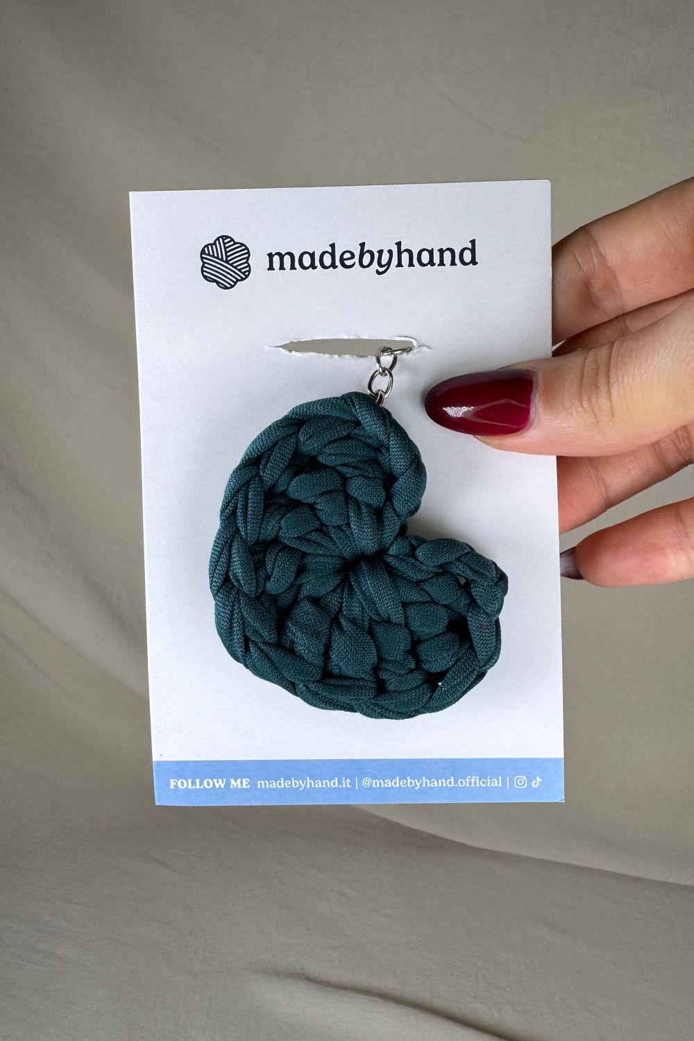 Portachiavi cuore petrolio Made By Hand, in fettuccia all’uncinetto, su cartoncino bianco con logo, ideale come bomboniera o piccolo dono fatto a mano