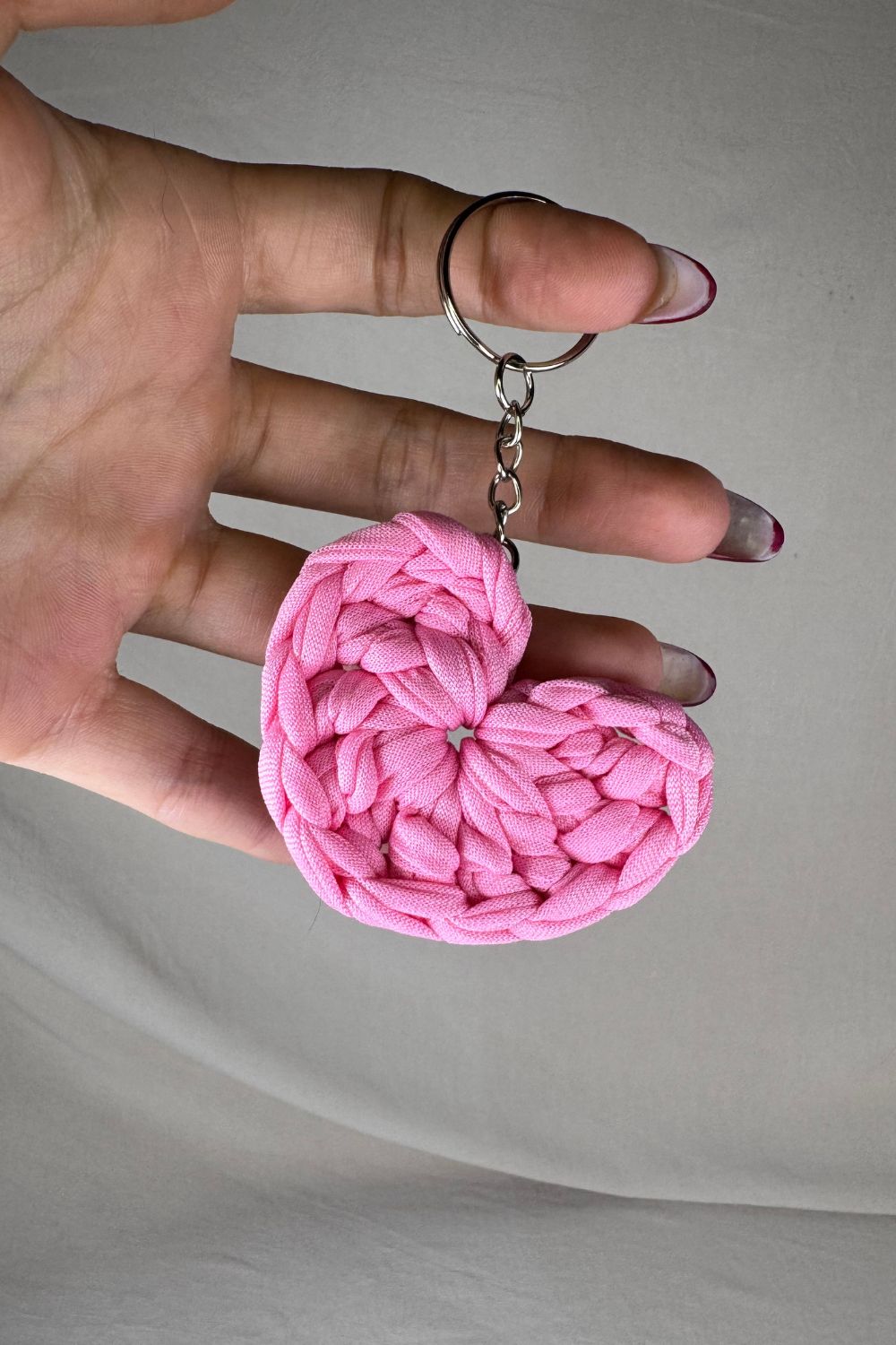 Portachiavi a cuore rosa in fettuccia lavorata all’uncinetto, fatto a mano in Italia da Made By Hand, mostrato in mano per evidenziare la delicatezza artigianale