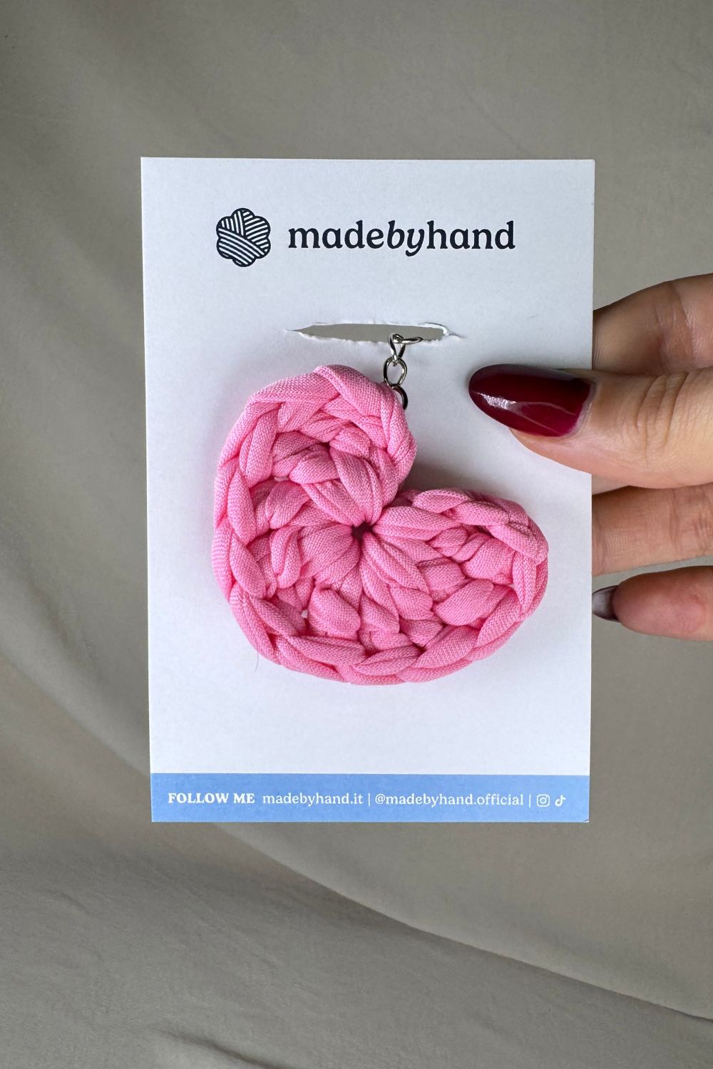 Portachiavi cuore rosa Made By Hand, in fettuccia all’uncinetto, confezionato su cartoncino bianco con logo, ideale come regalo dolce e romantico