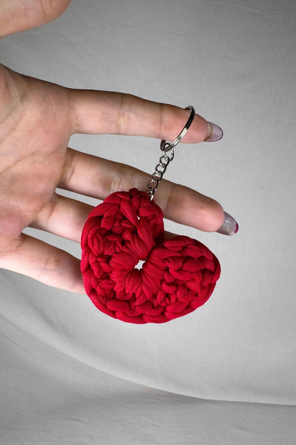 Portachiavi a cuore rosso realizzato all’uncinetto con fettuccia, fatto a mano in Italia da Made By Hand, mostrato in mano come simbolo di amore e artigianalità