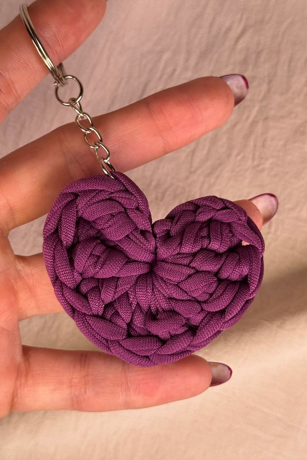 Portachiavi cuore viola in fettuccia lavorato all’uncinetto, fatto a mano in Italia da Made By Hand, mostrato in mano per evidenziare la dimensione reale