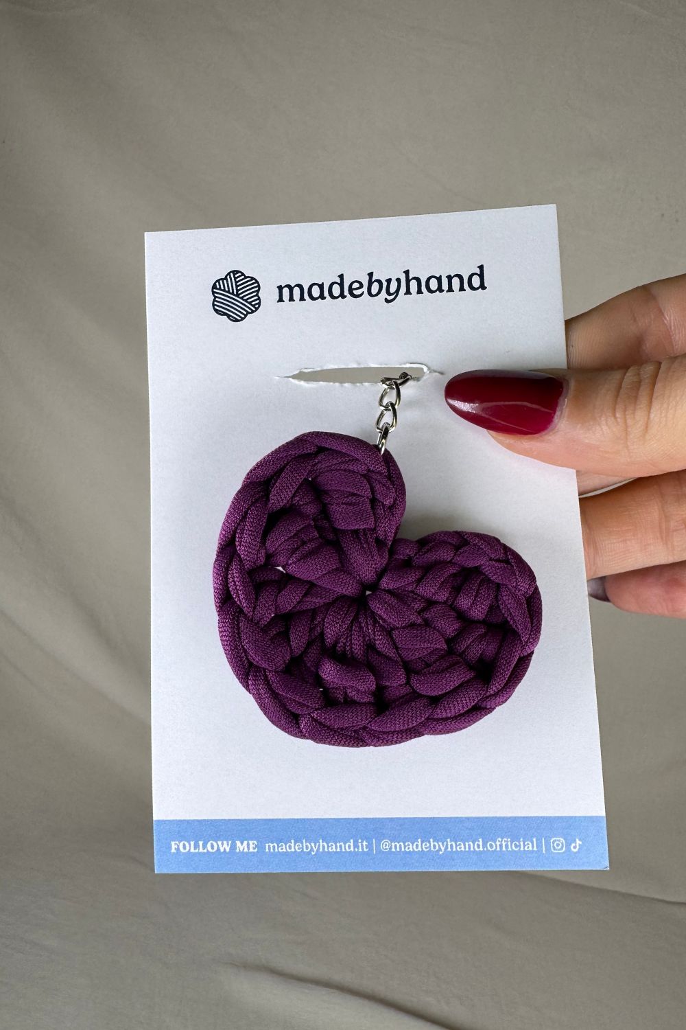 Portachiavi cuore viola Made By Hand, in fettuccia all’uncinetto, su cartoncino bianco con logo, perfetto come bomboniera o pensiero artigianale