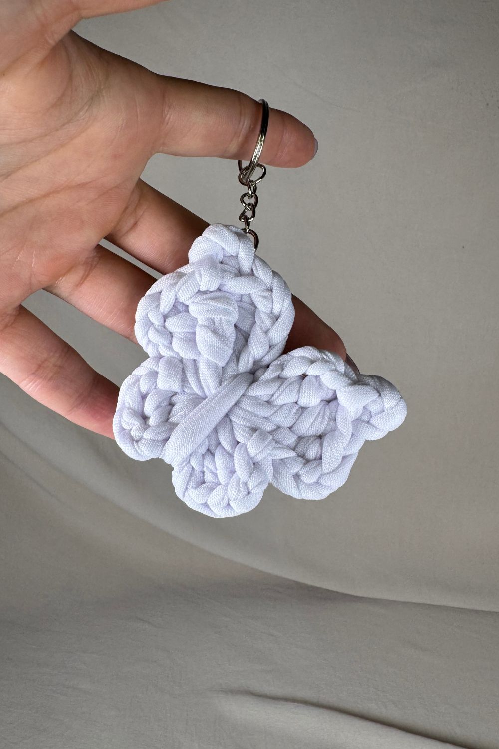 Portachiavi a forma di farfalla bianca lavorato all’uncinetto, fatto a mano in Italia da Made By Hand, mostrato in mano per evidenziare la misura reale
