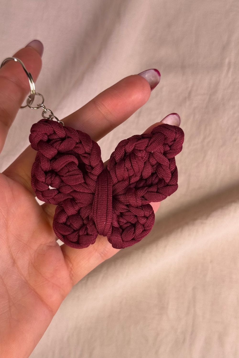 Portachiavi farfalla bordeaux lavorato all’uncinetto, realizzato a mano in Italia da Made By Hand, mostrato in mano per farne vedere i dettagli