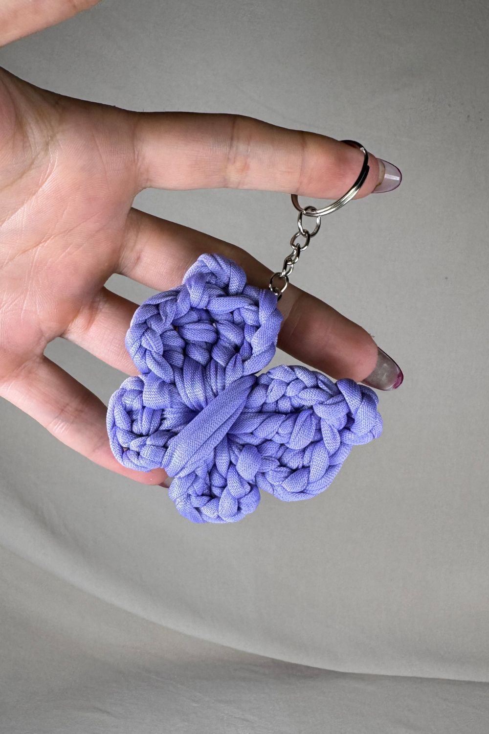 Portachiavi a farfalla lilla in cotone lavorato all’uncinetto, fatto a mano in Italia da Made By Hand, mostrato in mano per evidenziare la grandezza