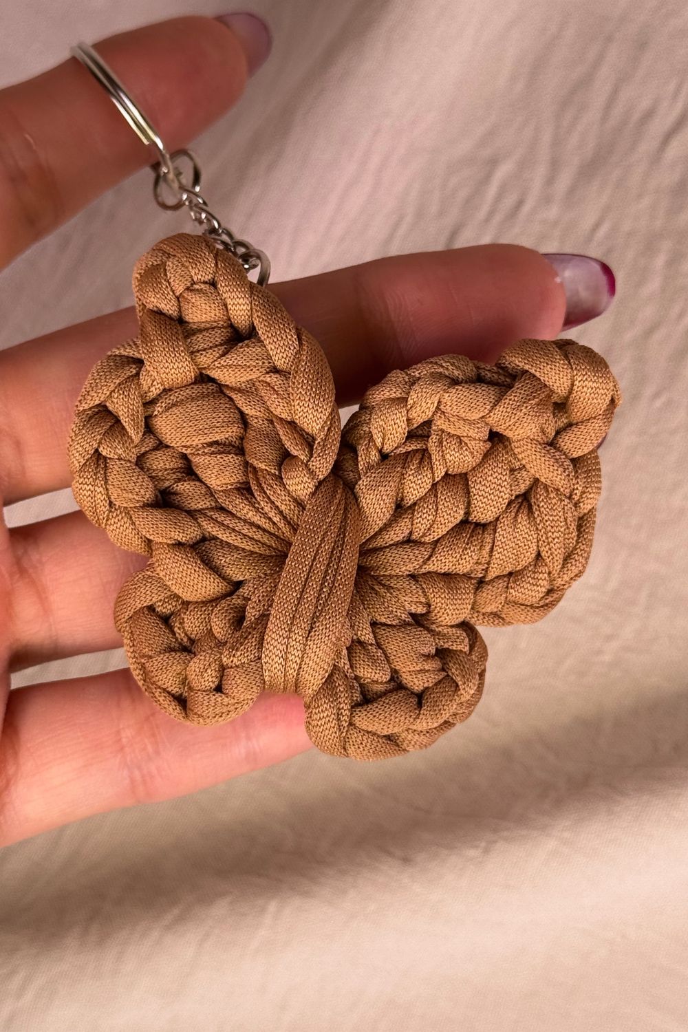 Portachiavi farfalla color nocciola realizzato all’uncinetto, fatto a mano in Italia da Made By Hand, mostrato in mano per mostrare le dimensioni reali