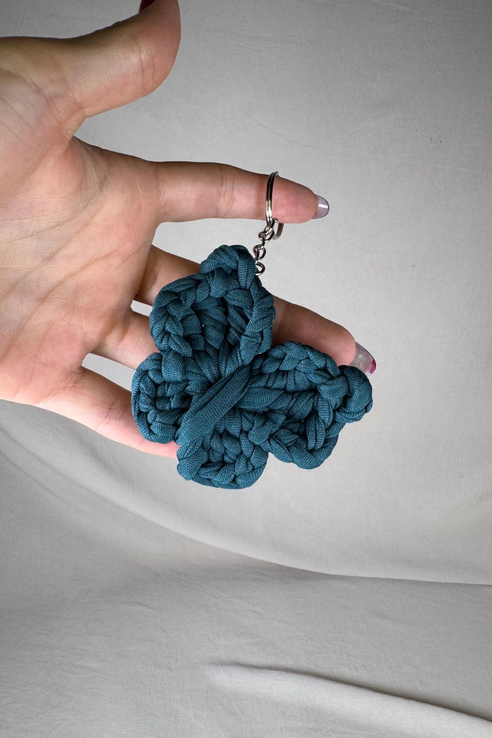 Portachiavi a farfalla color petrolio realizzato all’uncinetto, fatto a mano in Italia da Made By Hand, mostrato in mano per evidenziare i dettagli artigianali