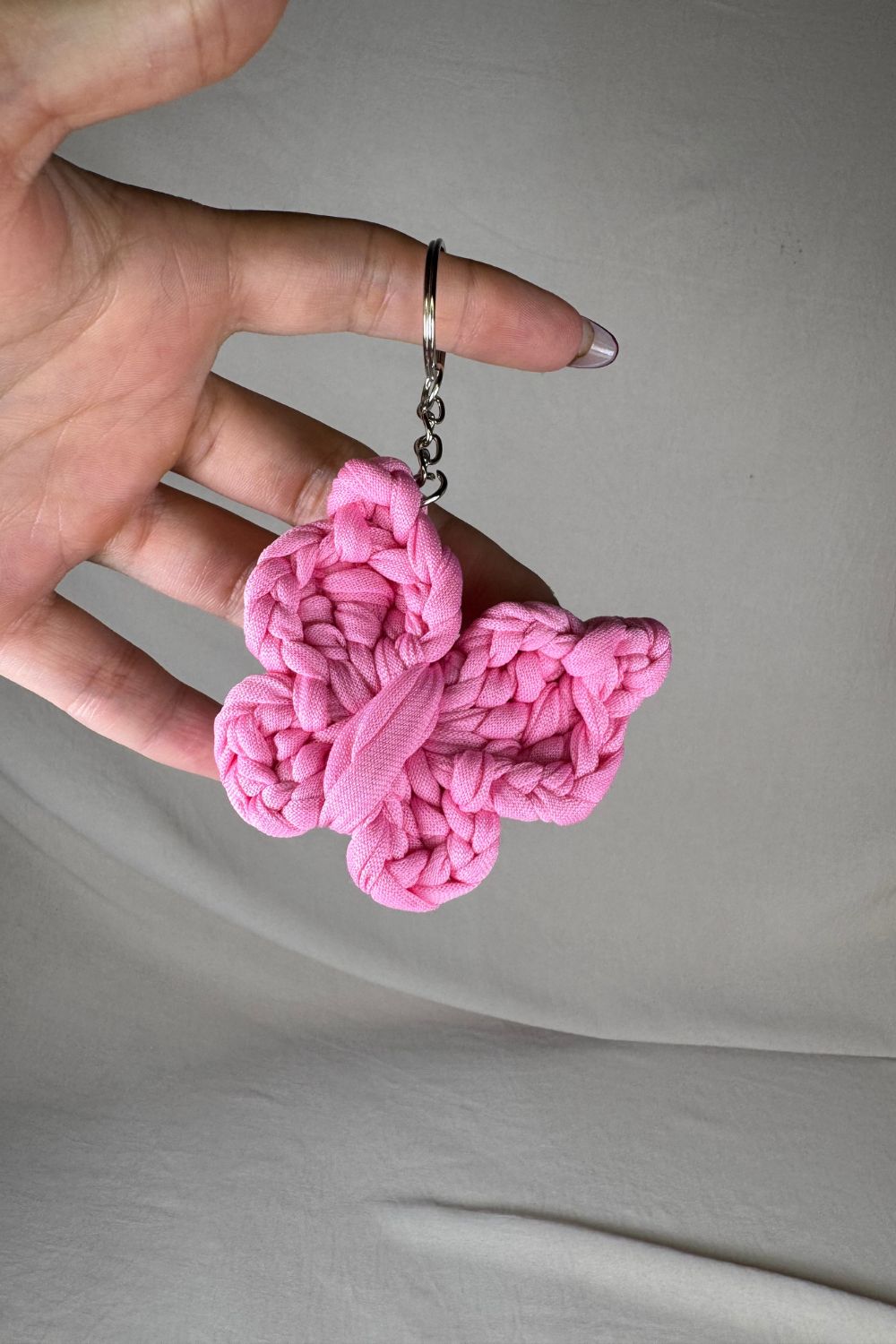 Portachiavi a forma di farfalla rosa lavorato all’uncinetto, fatto a mano in Italia da Made By Hand, mostrato in mano per dare un’idea della dimensione