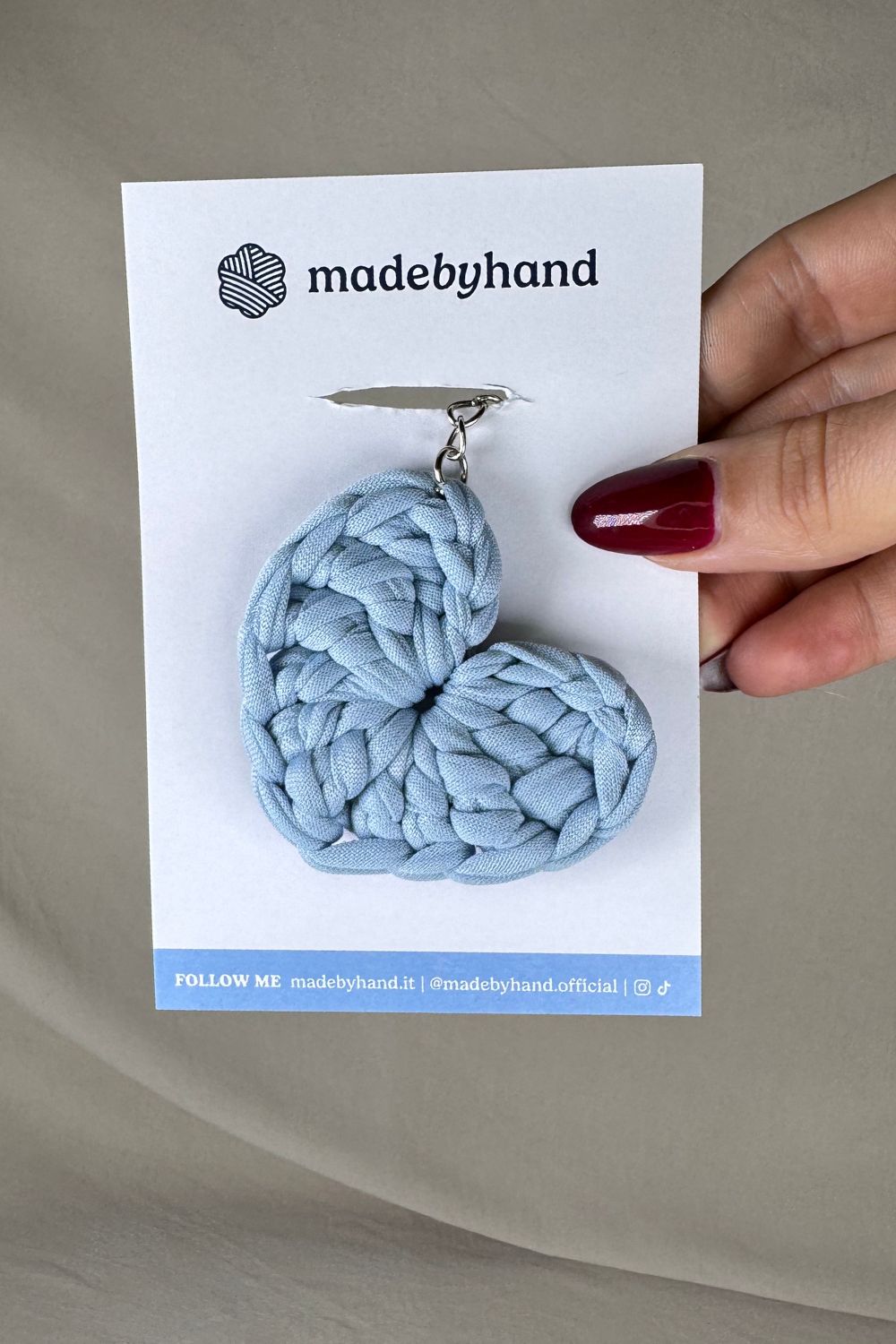 Portachiavi cuore azzurro all’uncinetto Made By Hand, confezionato su cartoncino bianco con logo, ideale come bomboniera o piccolo regalo artigianale