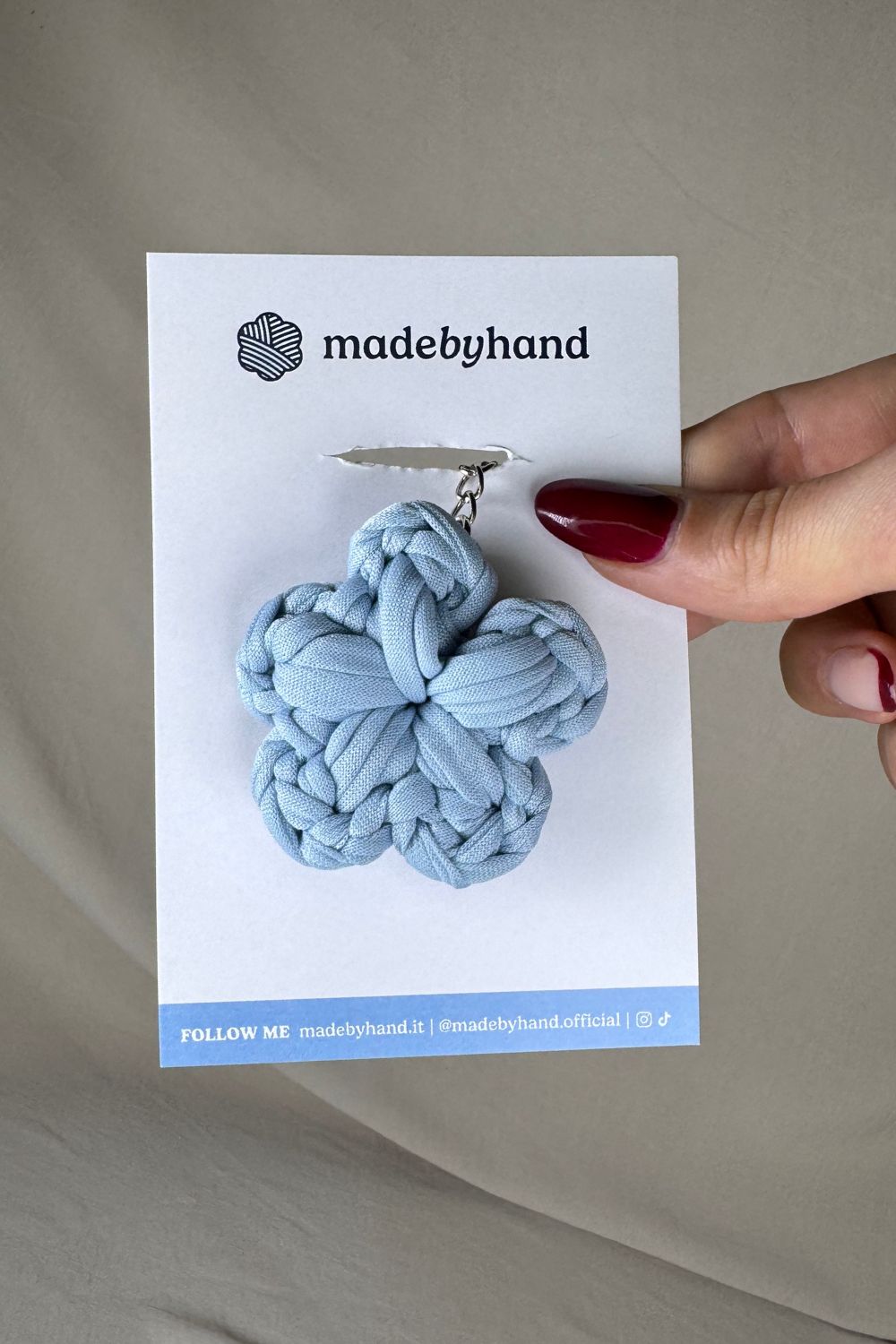 Portachiavi fiore azzurro all’uncinetto Made By Hand, confezionato su cartoncino bianco con logo, perfetto come bomboniera o piccolo regalo artigianale