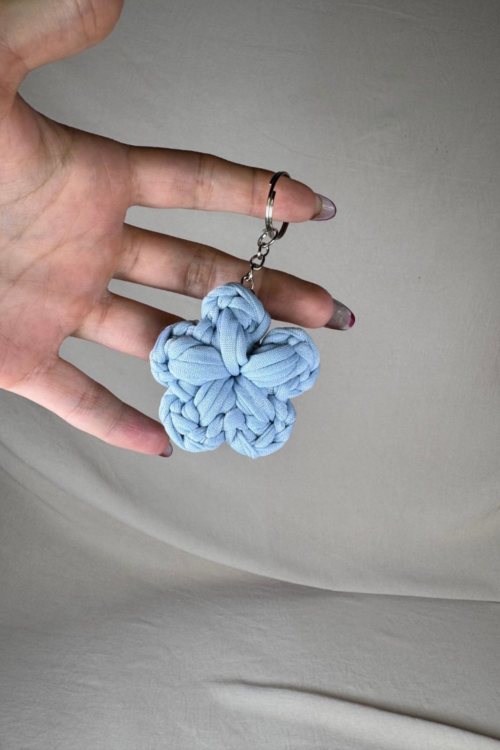 Portachiavi a forma di fiore azzurro realizzato all’uncinetto, fatto a mano in Italia da Made By Hand, mostrato in mano per evidenziarne le dimensioni