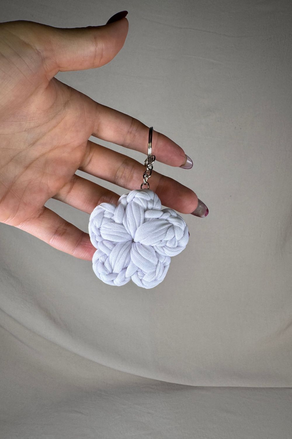 Portachiavi a fiore bianco in cotone lavorato all’uncinetto, fatto a mano in Italia da Made By Hand, mostrato in mano per mostrare la grandezza
