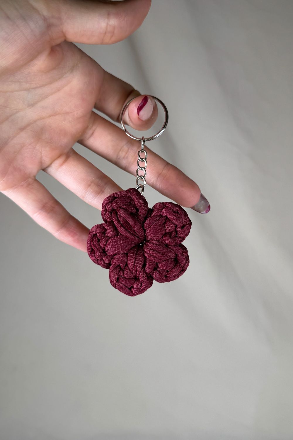 Portachiavi fiore bordeaux realizzato all’uncinetto, fatto a mano in Italia da Made By Hand, mostrato in mano per dare un’idea della misura reale