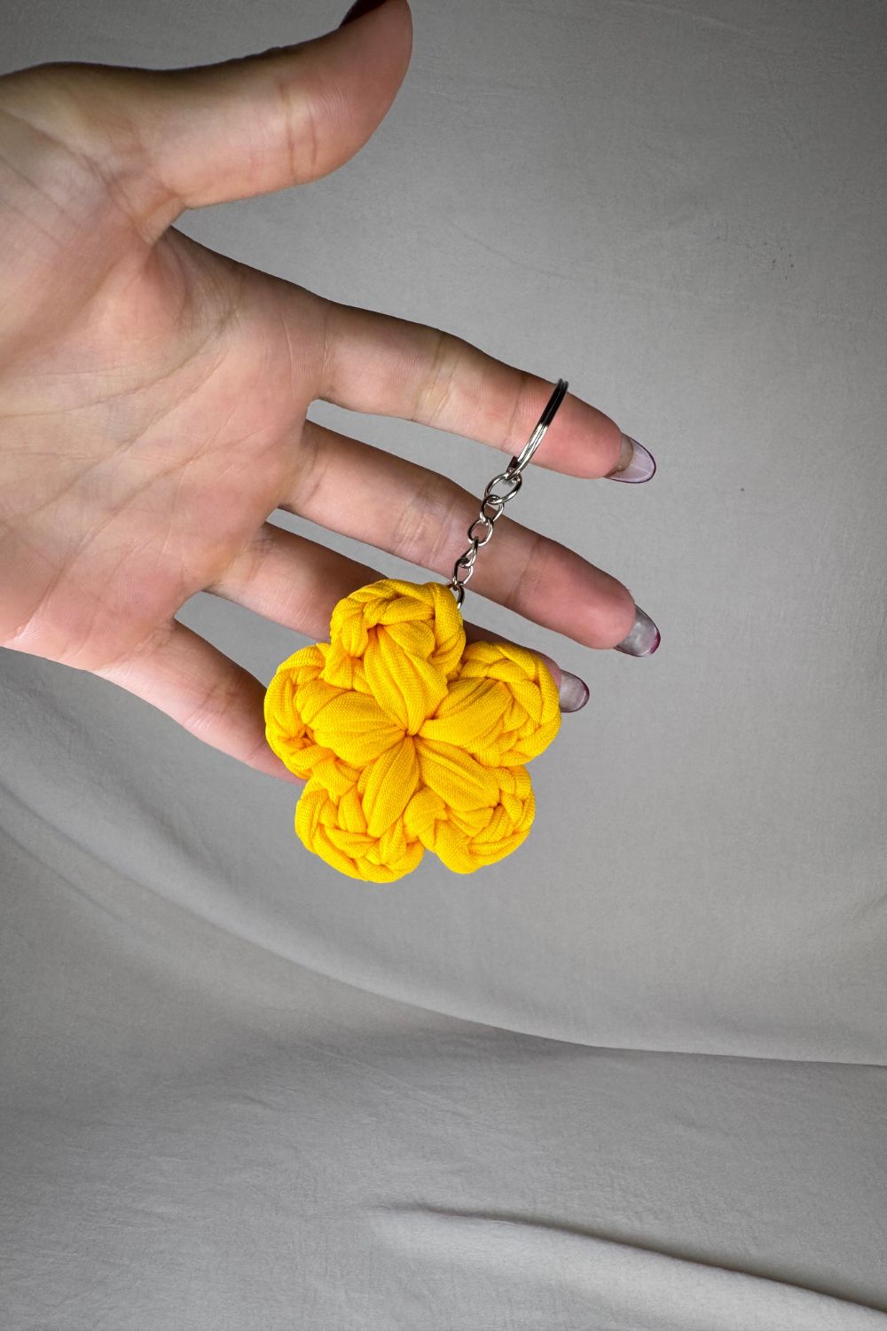 Portachiavi a fiore giallo lavorato all’uncinetto, fatto a mano in Italia da Made By Hand, mostrato in mano per evidenziare le dimensioni e i dettagli
