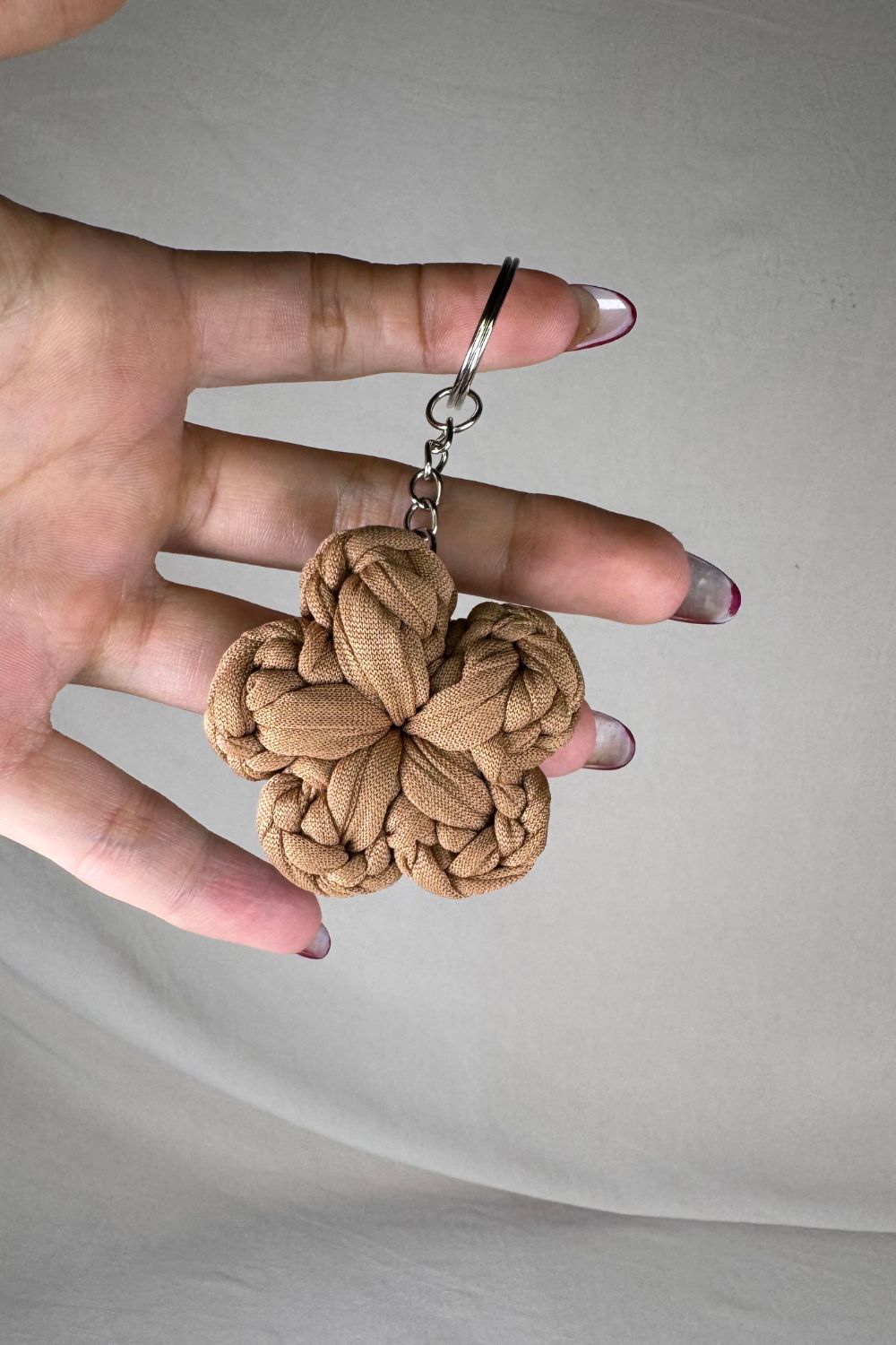 Portachiavi fiore color nocciola realizzato all’uncinetto, fatto a mano in Italia da Made By Hand, mostrato in mano per mostrare le proporzioni reali