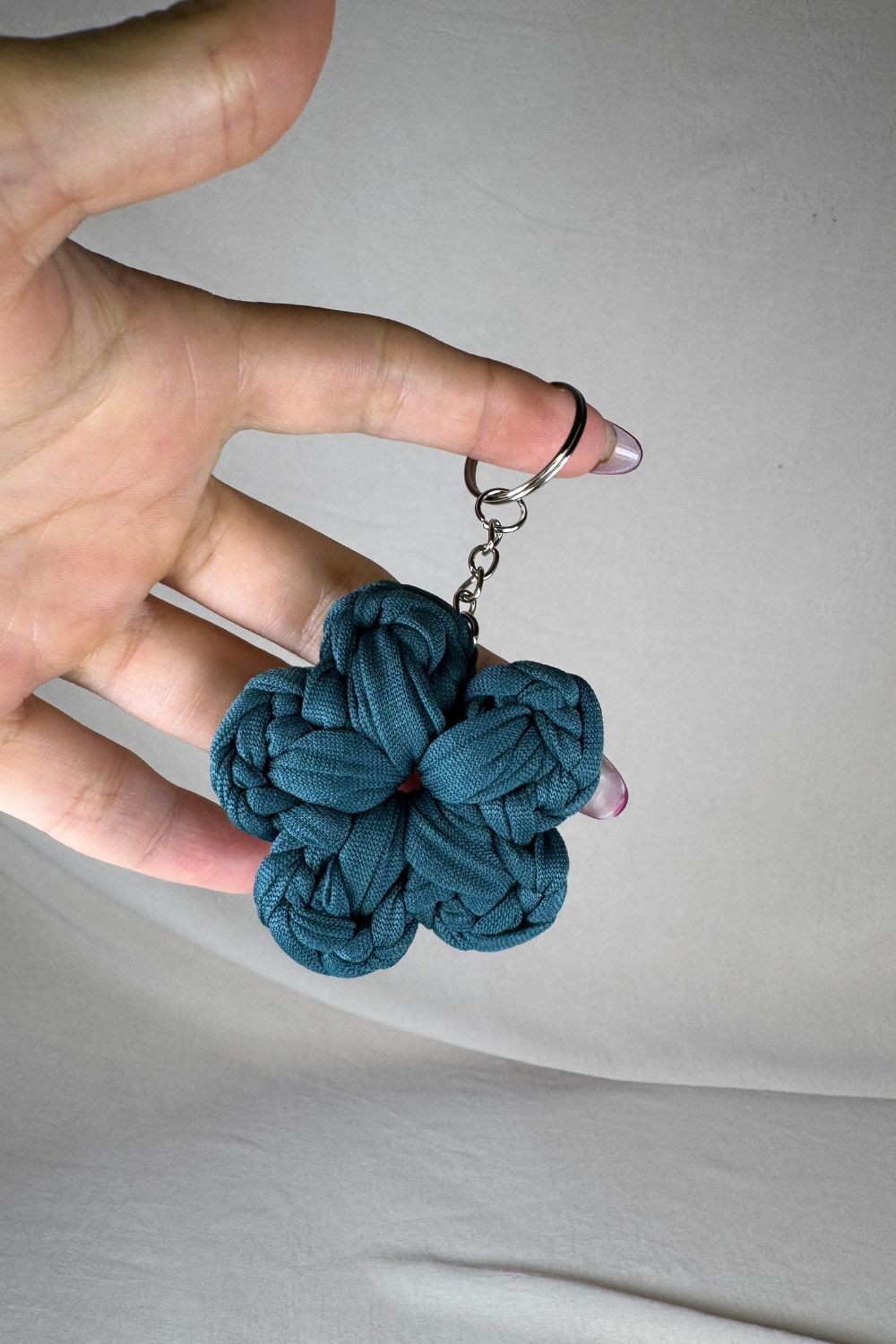 Portachiavi a fiore color petrolio realizzato all’uncinetto, fatto a mano in Italia da Made By Hand, mostrato in mano per evidenziare le dimensioni