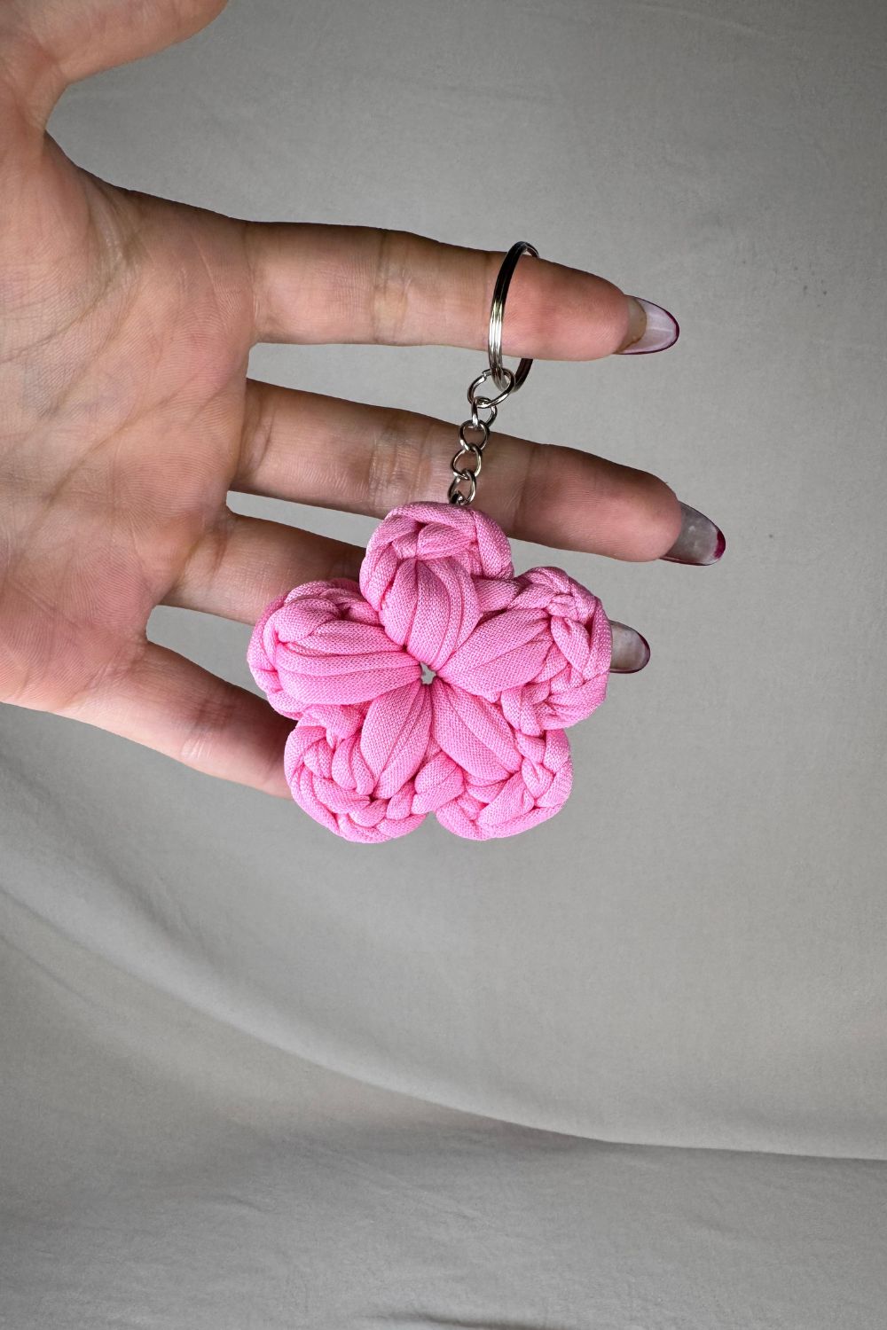 Portachiavi fiore rosa in fettuccia lavorata all’uncinetto, fatto a mano in Italia da Made By Hand, mostrato in mano per evidenziare la grandezza