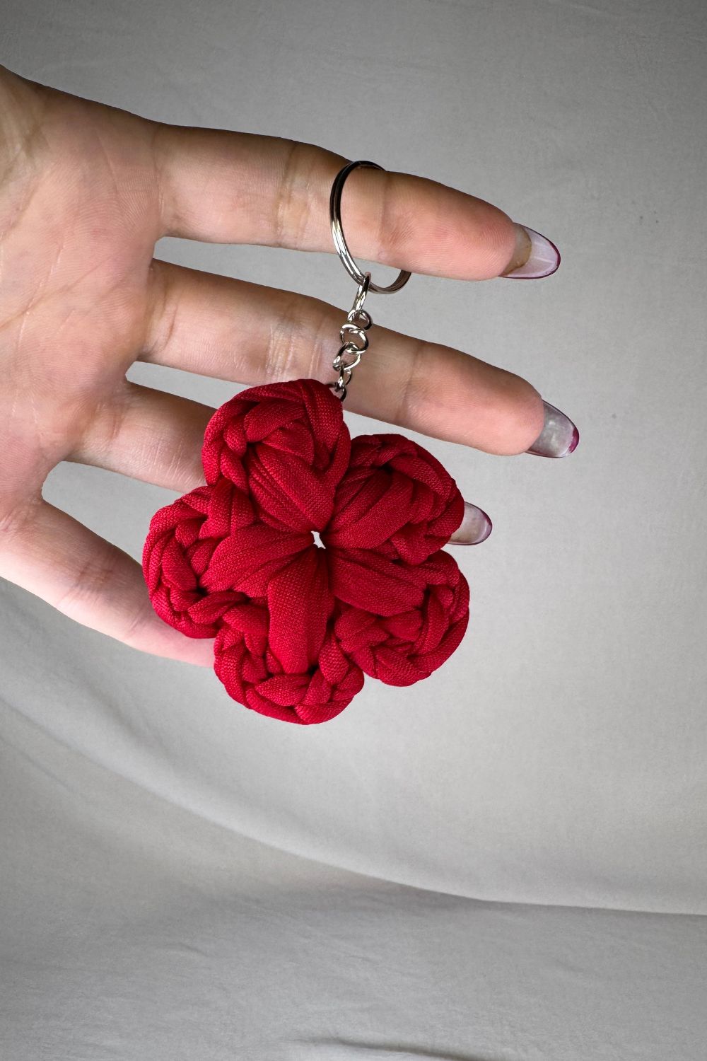 Portachiavi a fiore rosso realizzato all’uncinetto, fatto a mano in Italia da Made By Hand, mostrato in mano come simbolo d’amore e artigianalità