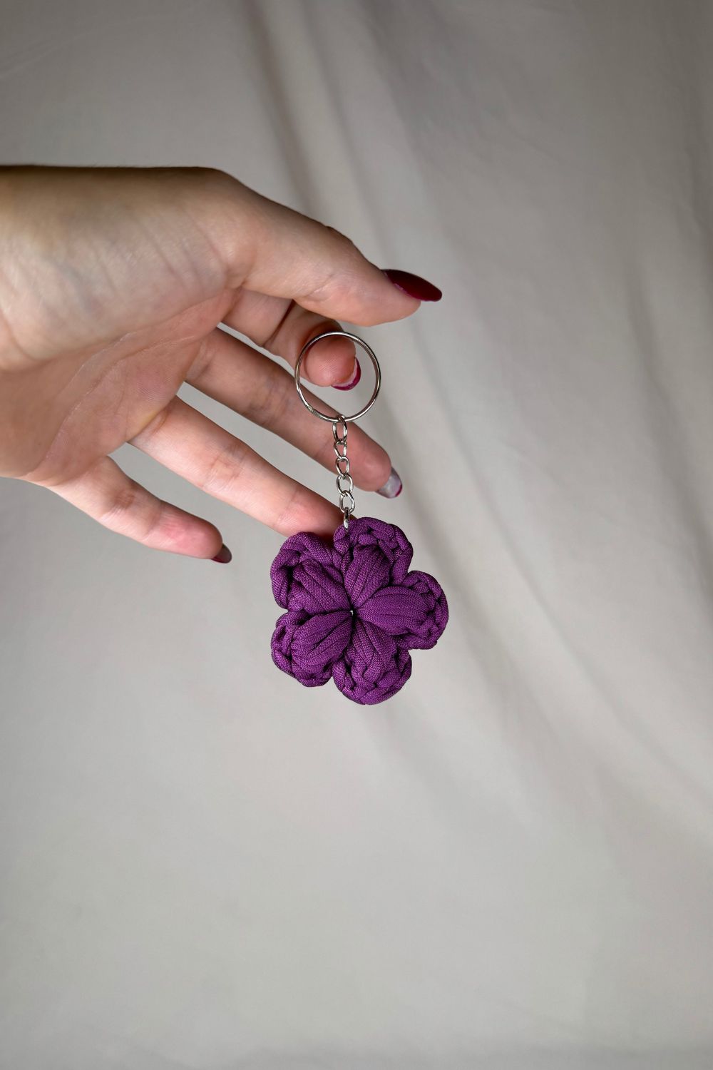 Portachiavi a fiore viola lavorato all’uncinetto, fatto a mano in Italia da Made By Hand, mostrato in mano per evidenziare la dimensione reale