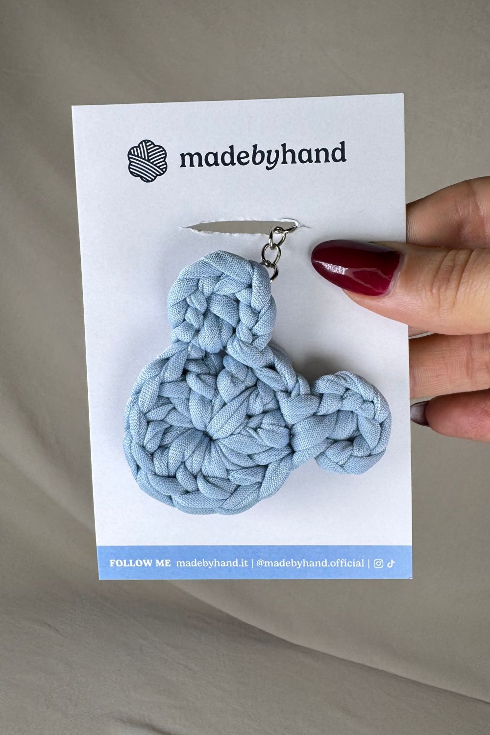 Portachiavi orsetto azzurro Made By Hand, all’uncinetto, confezionato su cartoncino bianco con logo, ideale come bomboniera o dono artigianale