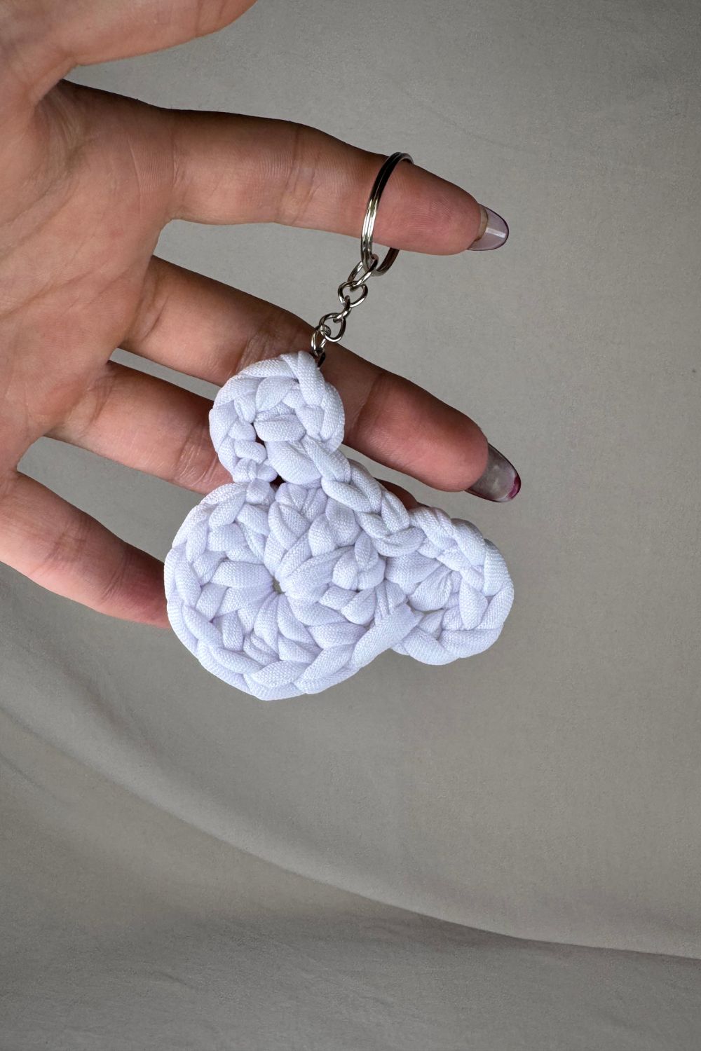 Portachiavi orsetto bianco in cotone lavorato all’uncinetto, fatto a mano in Italia da Made By Hand, mostrato in mano per dare un’idea della misura