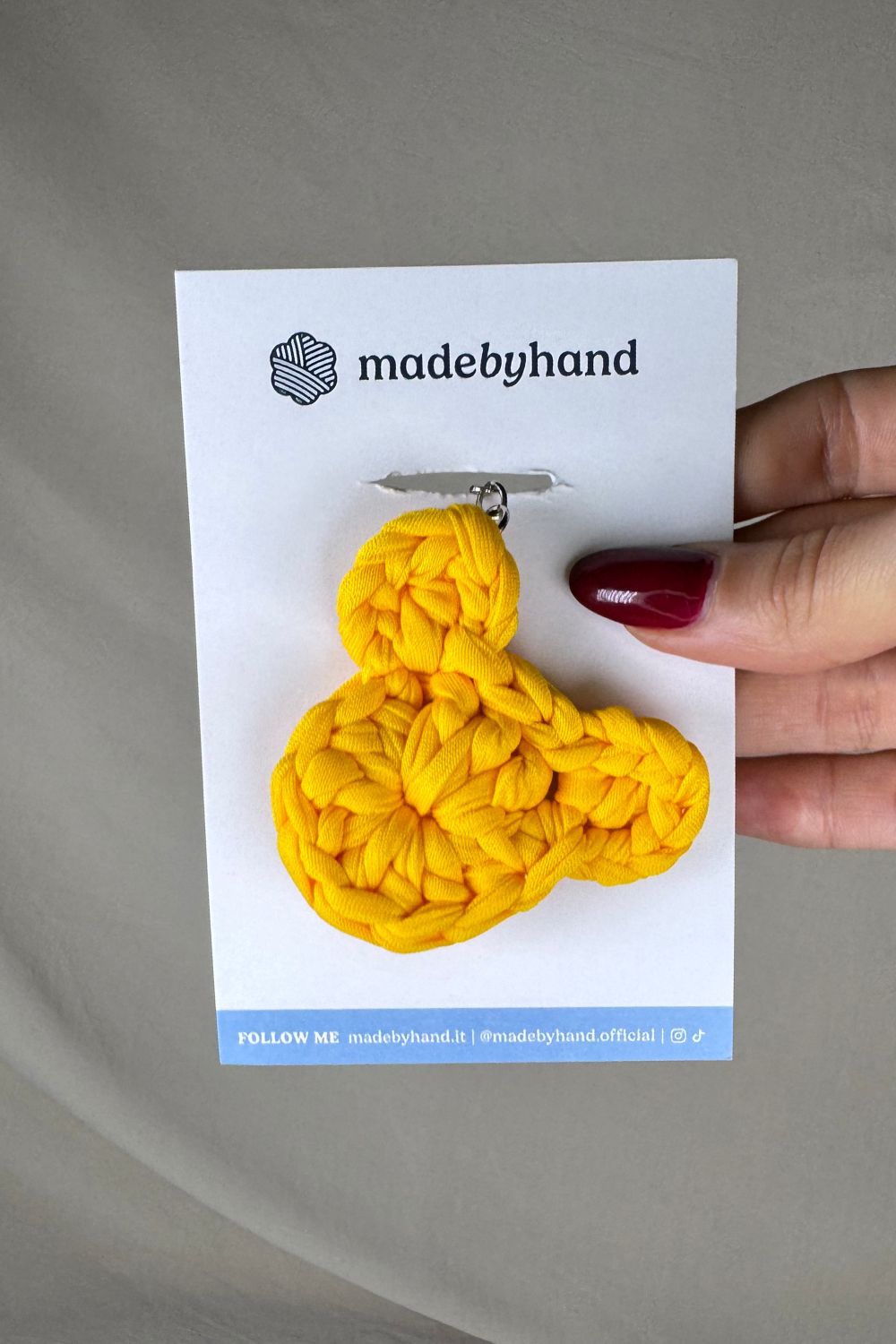 Portachiavi orsetto giallo all’uncinetto Made By Hand, confezionato su cartoncino bianco con logo, allegro e luminoso, perfetto come bomboniera o dono artigianale