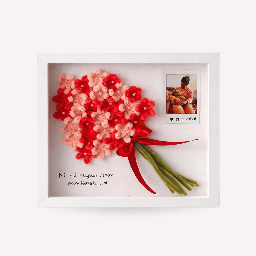 Quadro ricordo artigianale con cornice bianca, bouquet di fiori rosa e rossi realizzati a mano, fiocco rosso e steli verdi. All’interno è presente una foto personalizzata e una dedica scritta, ideale come regalo emotivo e decorativo.