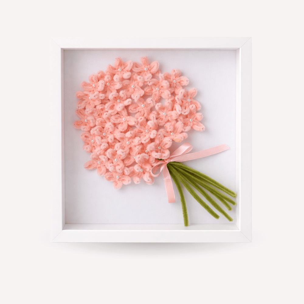 Quadro ricordo artigianale con cornice bianca, bouquet di fiori rosa fatti a mano con piccoli dettagli luminosi, fiocco rosa e steli verdi. Decorazione elegante e personalizzabile, adatta come idea regalo per la festa della mamma o della donna o complemento d’arredo