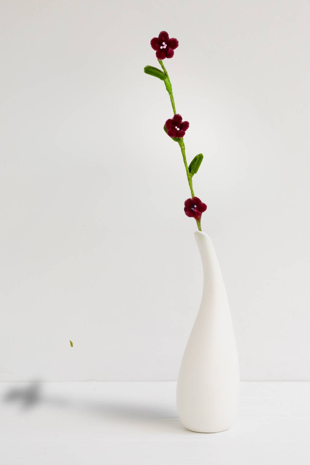 In un vaso, un rametto con 3 mini margherite bordeaux in scovolini, fatto a mano da Made By Hand in Italia, fiore artigianale decorativo 34 cm ideale per mazzi o regali floreali sostenibili. Made by hand crea fiori con scovolini colorati fatti a mano in italia.