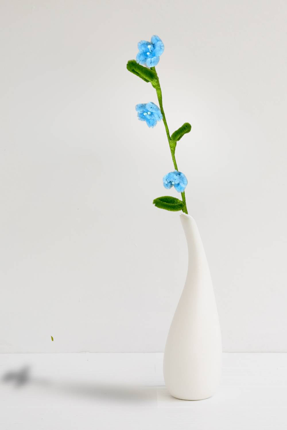In un vaso, un rametto con 3 mini margherite azzurre in scovolini, fatto a mano da Made By Hand in Italia, fiore artigianale decorativo 34 cm ideale per mazzi o regali floreali sostenibili. Made by hand crea fiori con scovolini colorati fatti a mano in italia.