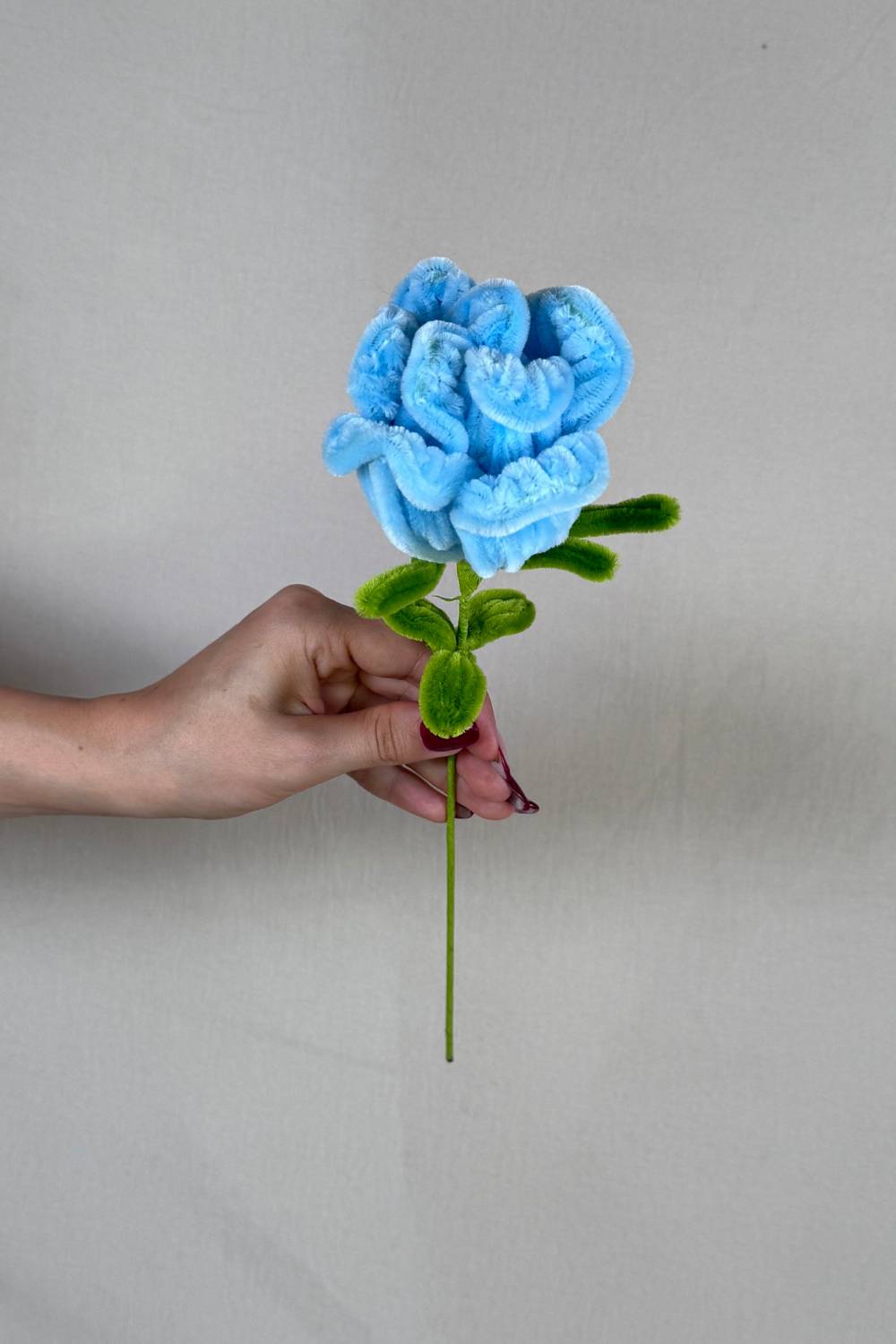 Rosa azzurra in scovolini artigianale Made By Hand tenuta in mano per mostrare le dimensioni reali, fiore fatto a mano con cura e materiali di qualità. Made By Hand crea fiori fatti con scovolini a mano in Italia