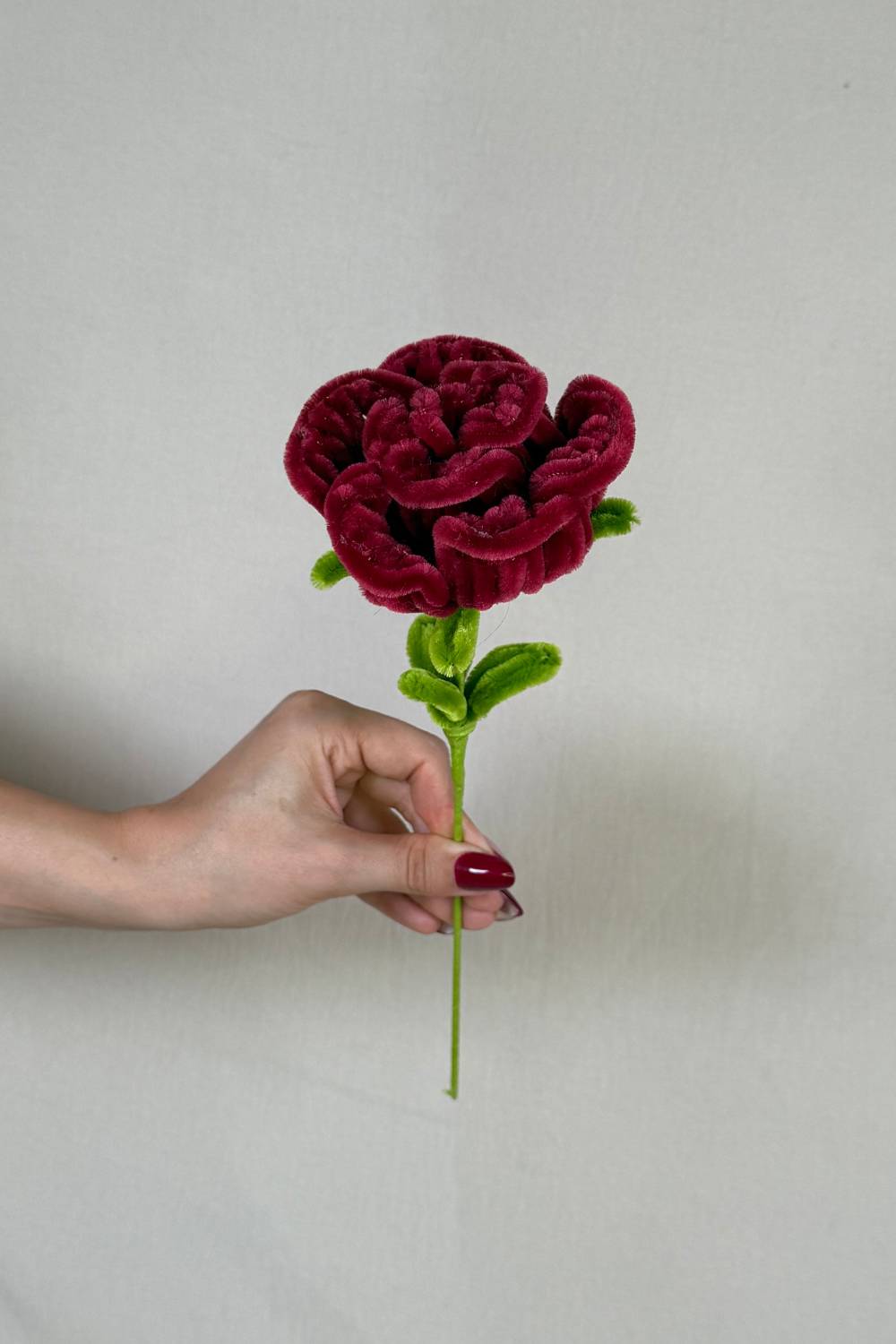 Rosa bordeaux in scovolini artigianale Made By Hand tenuta in mano per mostrare le dimensioni reali, fiore fatto a mano con cura e materiali di qualità. Made By Hand crea kit e  fiori fatti con scovolini a mano in Italia