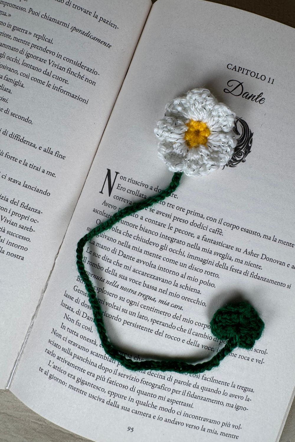 Segnalibro margherita all’uncinetto Made By Hand inserito tra le pagine di un libro, accessorio artigianale floreale fatto a mano in Italia, simbolo di amore per la lettura e per l’artigianato.