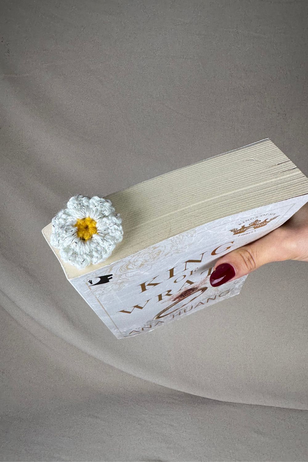 Segnalibro margherita all’uncinetto artigianale Made By Hand tenuto in  un libro chiuso in mano per mostrare le dimensioni, realizzato con filato di cotone di qualità e lavorazione italiana fatta a mano.