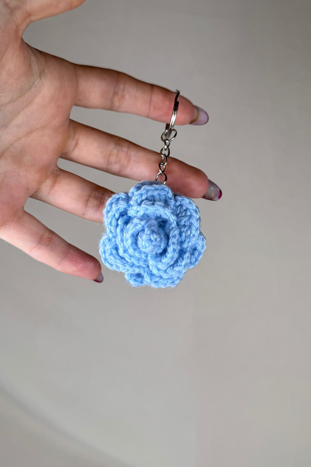 Portachiavi con rosa azzurra fatto a mano in Italia da Made By Hand, creazione artigianale in miniatura con fiore rosa all’uncinetto, mostrato in mano per evidenziare i dettagli e le dimensioni